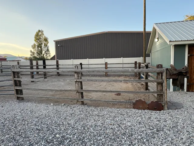 Gravel lot with a four-rail wooden fence and a light blue outbuilding featuring a metal roof