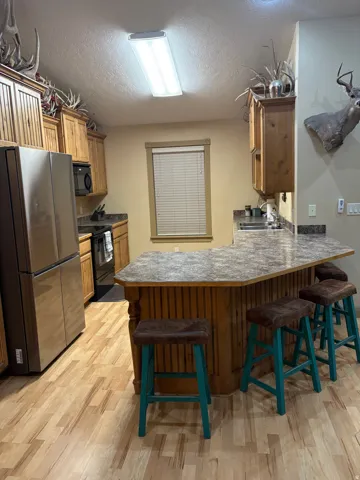 Kitchen featuring wood-finish flooring, stainless steel refrigerator, wood cabinetry, and a peninsula with a patterned countertop