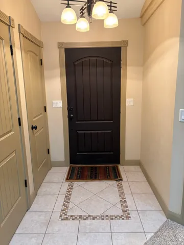 Recessed panel interior doors, decorative door trim, tiled flooring with mosaic border, dark wood-finish entry door, and a multi-light chandelier