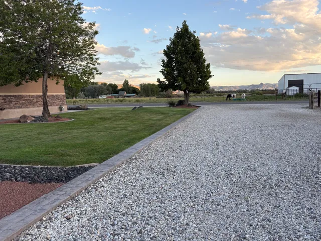 Extensive gravel driveway with a paver border, manicured lawn, and mature trees