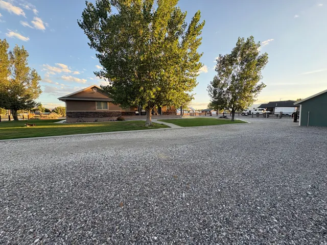 Spacious gravel driveway with a manicured lawn, established trees, and a visible building structure