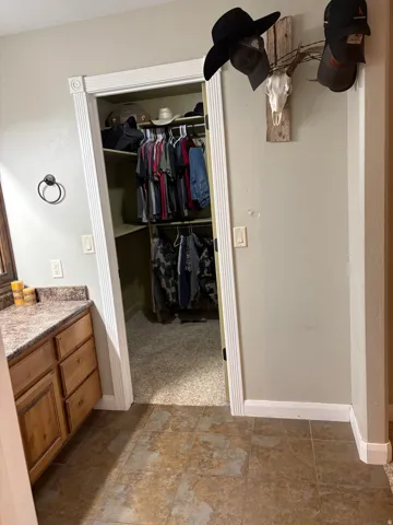 Walk-in closet with built-in shelving, wood-finish vanity with granite-style countertop, and tiled flooring
