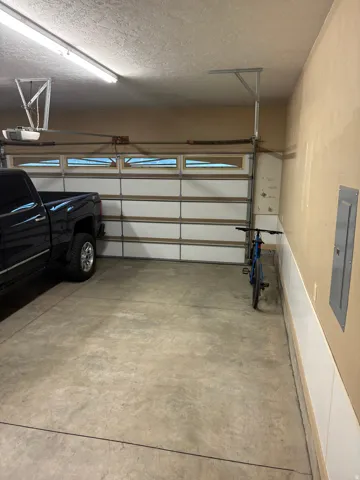 Garage space featuring concrete flooring, a white paneled garage door with windows, and a fluorescent ceiling light fixture