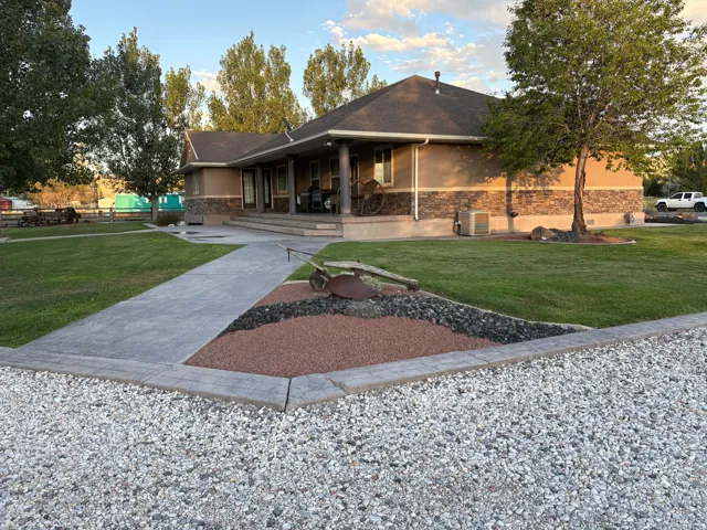 Stucco and stone exterior, covered porch with columns, well-maintained lawn, decorative rock landscaping, and a gravel driveway