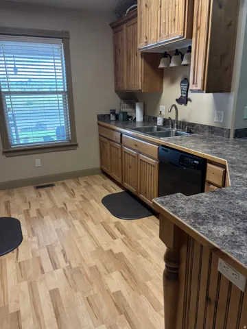 Wood-finish flooring, wood cabinetry, laminate countertops, stainless steel sink, and a built-in dishwasher