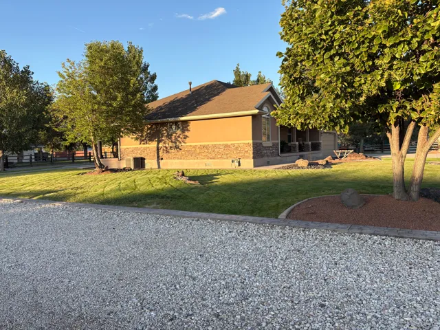 Exterior with a gravel driveway, mature trees, and a concrete-edged landscape bed