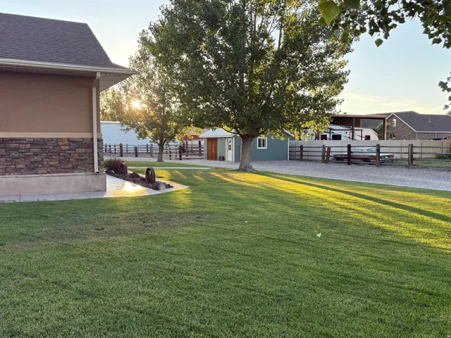 Spacious lawn area with mature trees, a gravel driveway, and wood fencing