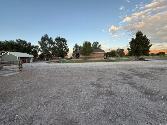 Expansive gravel-surfaced property featuring a single-story residence with a stone accent facade and a separate outbuilding with a metal roof