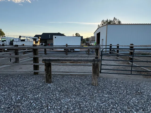 Gravel ground cover with wood post fencing, a metal gate, and a metal-sided building