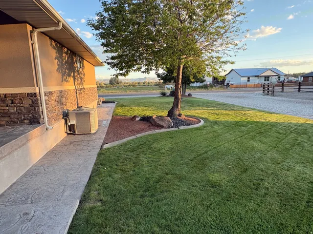 Stamped concrete pathway, stone veneer facade, manicured lawn, mature tree, and gravel driveway