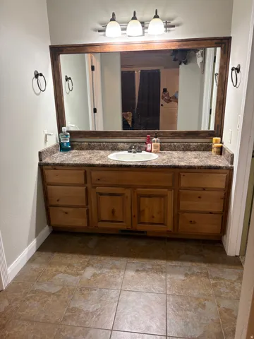 Wood-finish vanity with ample storage, a single basin sink, and a laminate countertop