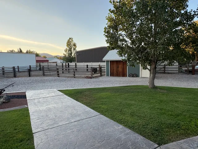 Manicured lawn with a stamped concrete pathway, gravel ground cover, and a detached outbuilding with a metal roof and wood paneling
