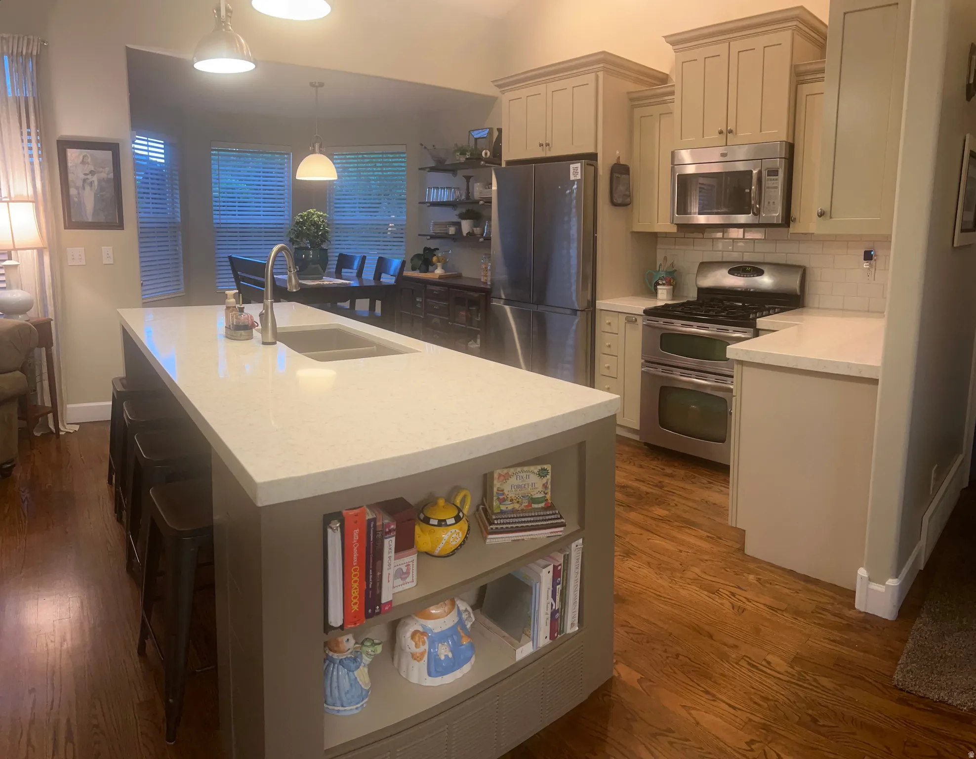 Kitchen featuring a large island with an undermount sink and built-in shelving, wood-finish flooring, stainless steel appliances, and cream-colored cabinetry