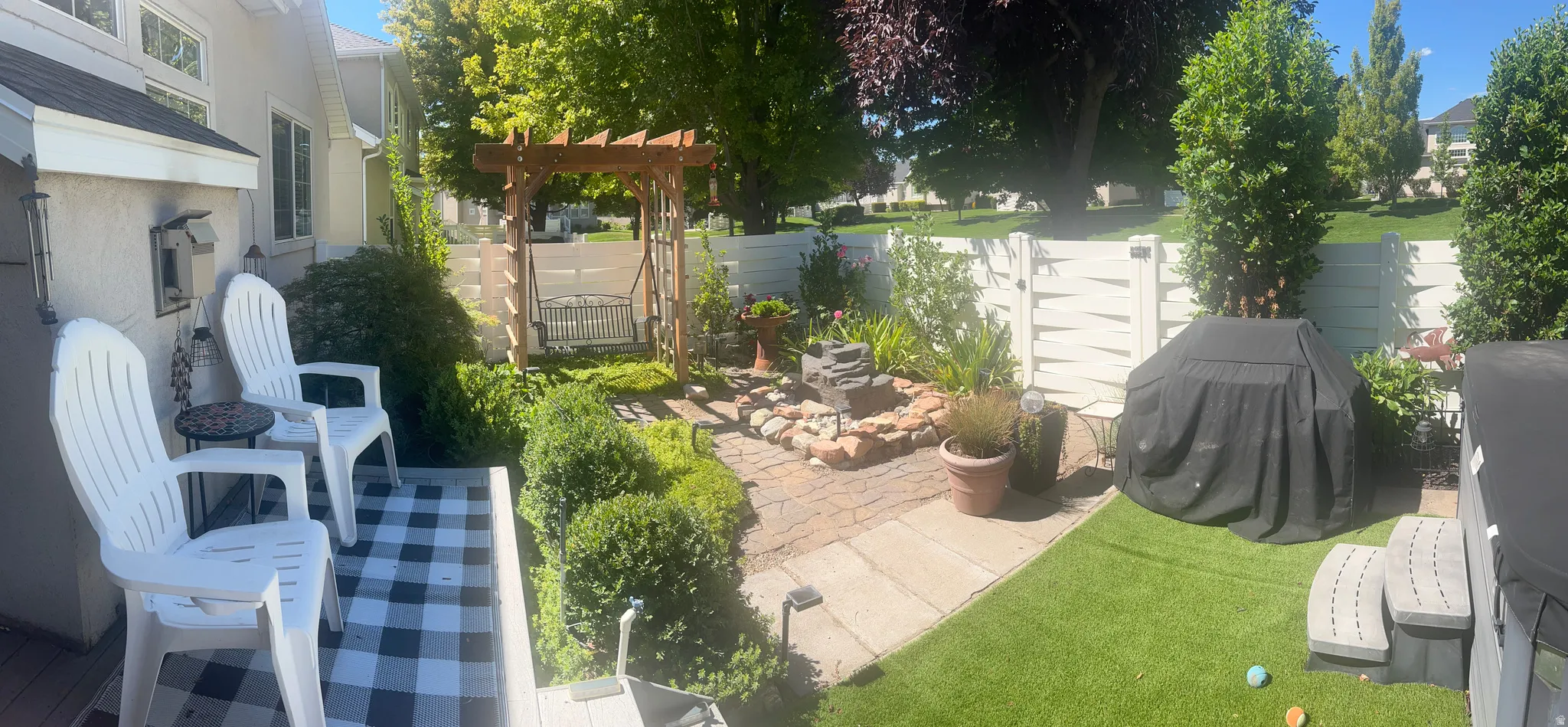 Manicured backyard featuring a paver patio, artificial turf, a wood pergola with a swing, and a decorative water feature