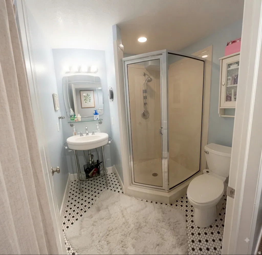 Bathroom featuring black and white hexagonal tile flooring, pedestal sink, glass-enclosed corner shower, and wall-mounted storage cabinet