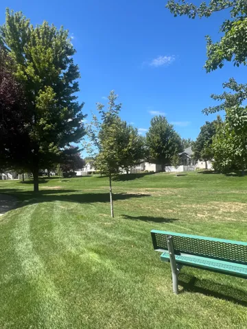 Expansive green space featuring mature trees and a dedicated park bench