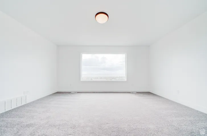 White painted walls, gray carpet, and a single window with a white frame