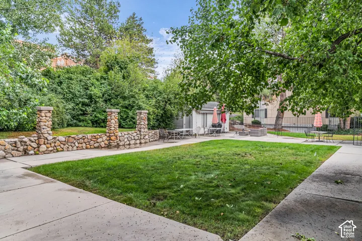 Lush green lawn with mature trees, stone wall and pillars, and concrete pathways