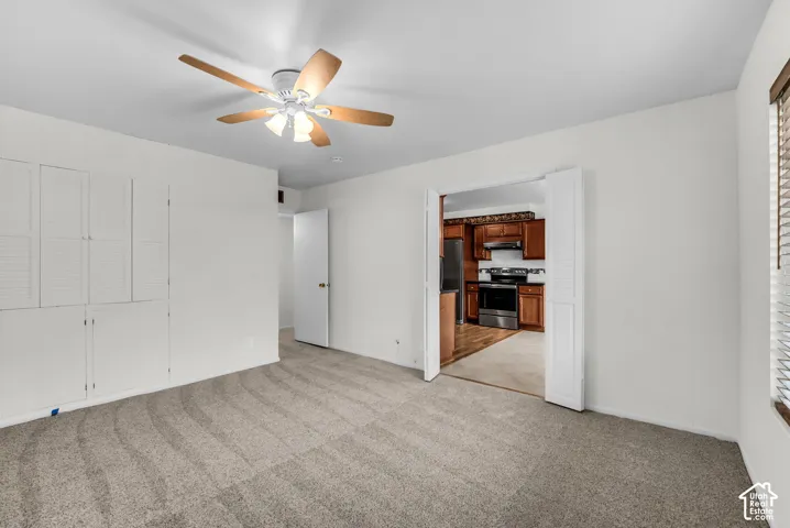 Recessed built-in cabinetry, ceiling fan with light fixture, carpeted flooring, and a kitchen with wood-finish cabinetry and stainless steel appliances