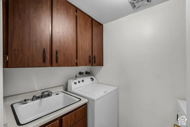 Utility sink with dual-handle faucet, wood-finish cabinetry, and overhead ventilation