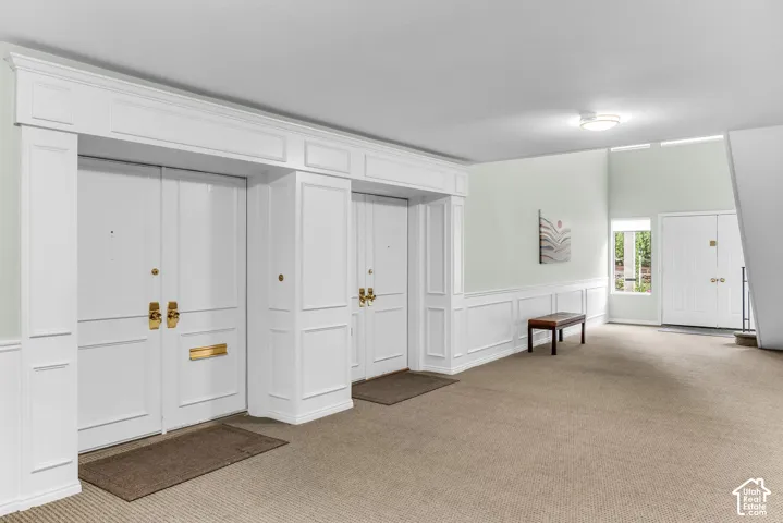 Interior entry area featuring wainscoting, a high vaulted ceiling, and carpeted flooring