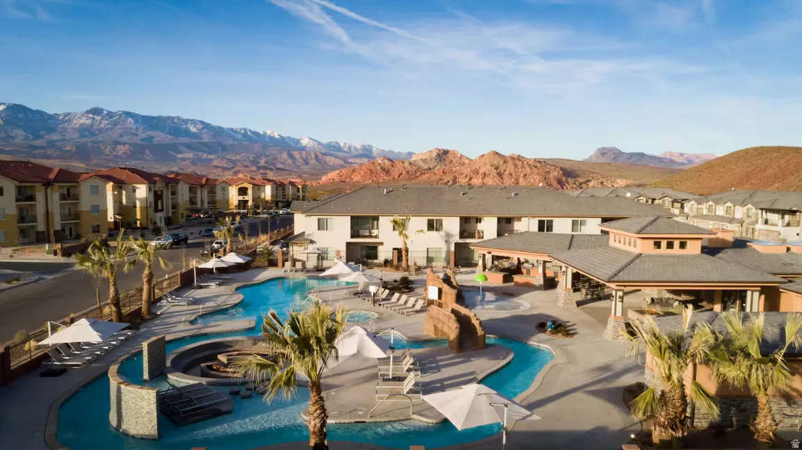 Expansive resort-style swimming pool, covered outdoor lounge area, multiple shade umbrellas, and desert mountain backdrop