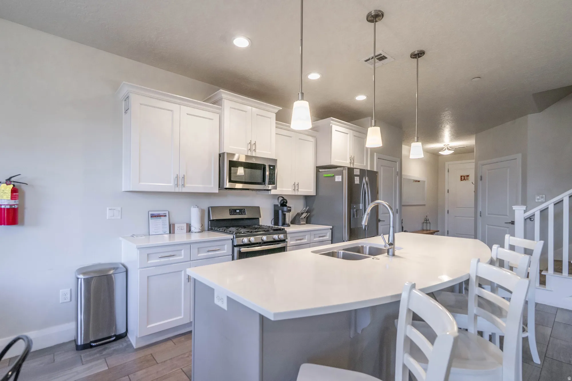 Kitchen featuring stainless steel appliances, white shaker-style cabinetry, a large kitchen island with integrated sink, pendant lighting, and wood-finish flooring