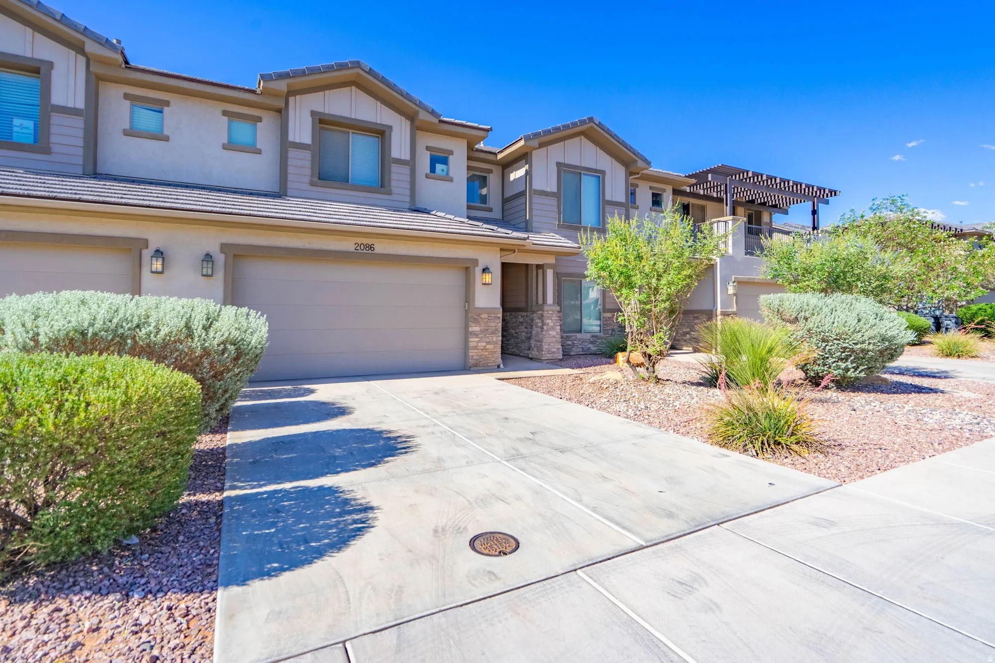 Striking two-story residence featuring a three-car garage, decorative concrete driveway with integrated drainage, and professionally landscaped front grounds with native desert plantings, ornamental shrubs, and rock hardscaping