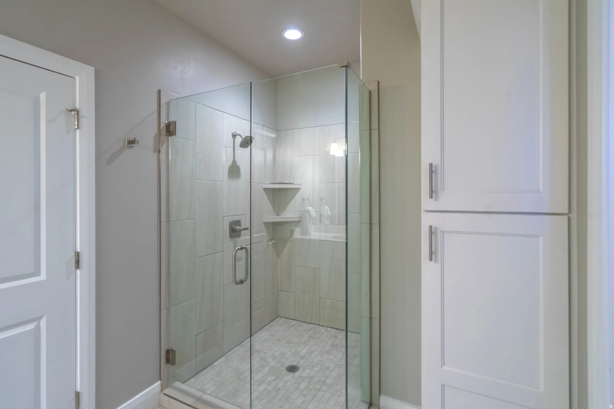 Glass-enclosed shower with tile surround and integrated shelving