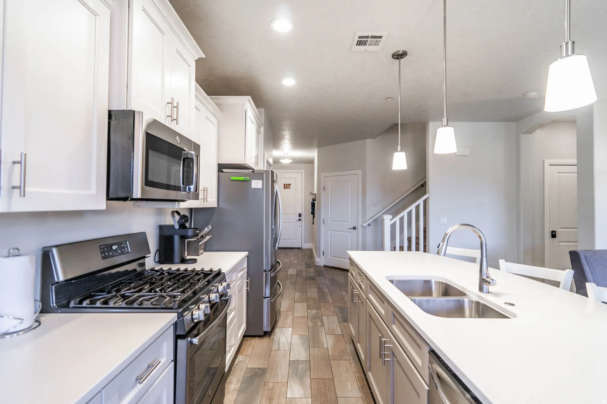 Kitchen featuring stainless steel appliances, white cabinetry, a kitchen island with a double basin sink, recessed lighting, and wood-finish flooring