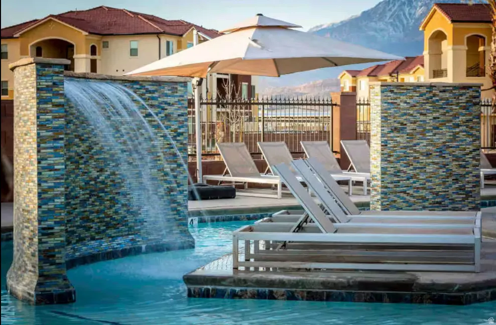 Swimming pool with a decorative waterfall feature, surrounding lounge seating, and a large shade umbrella