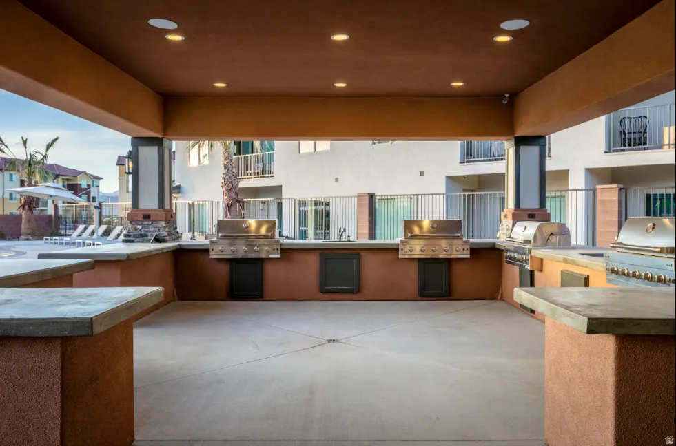 Covered outdoor kitchen area with multiple built-in grills, integrated counter space, and recessed lighting