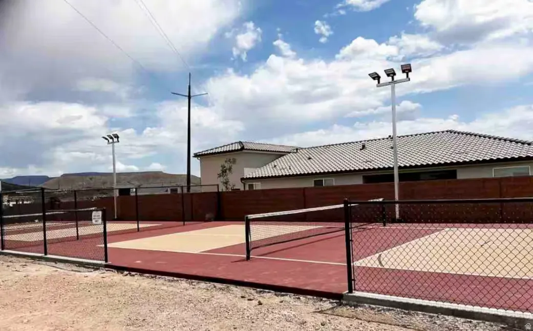 Outdoor sports court featuring a red and beige playing surface, black chain-link fencing, and integrated court lighting