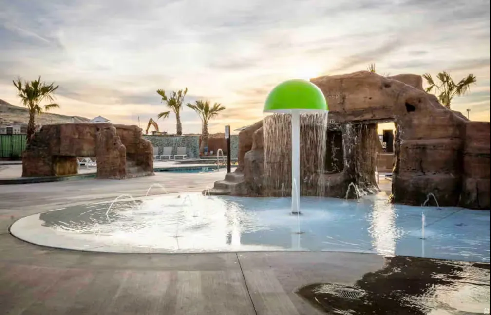 Water feature with a mushroom-shaped sprayer, integrated rock structures, and multiple ground-level water jets