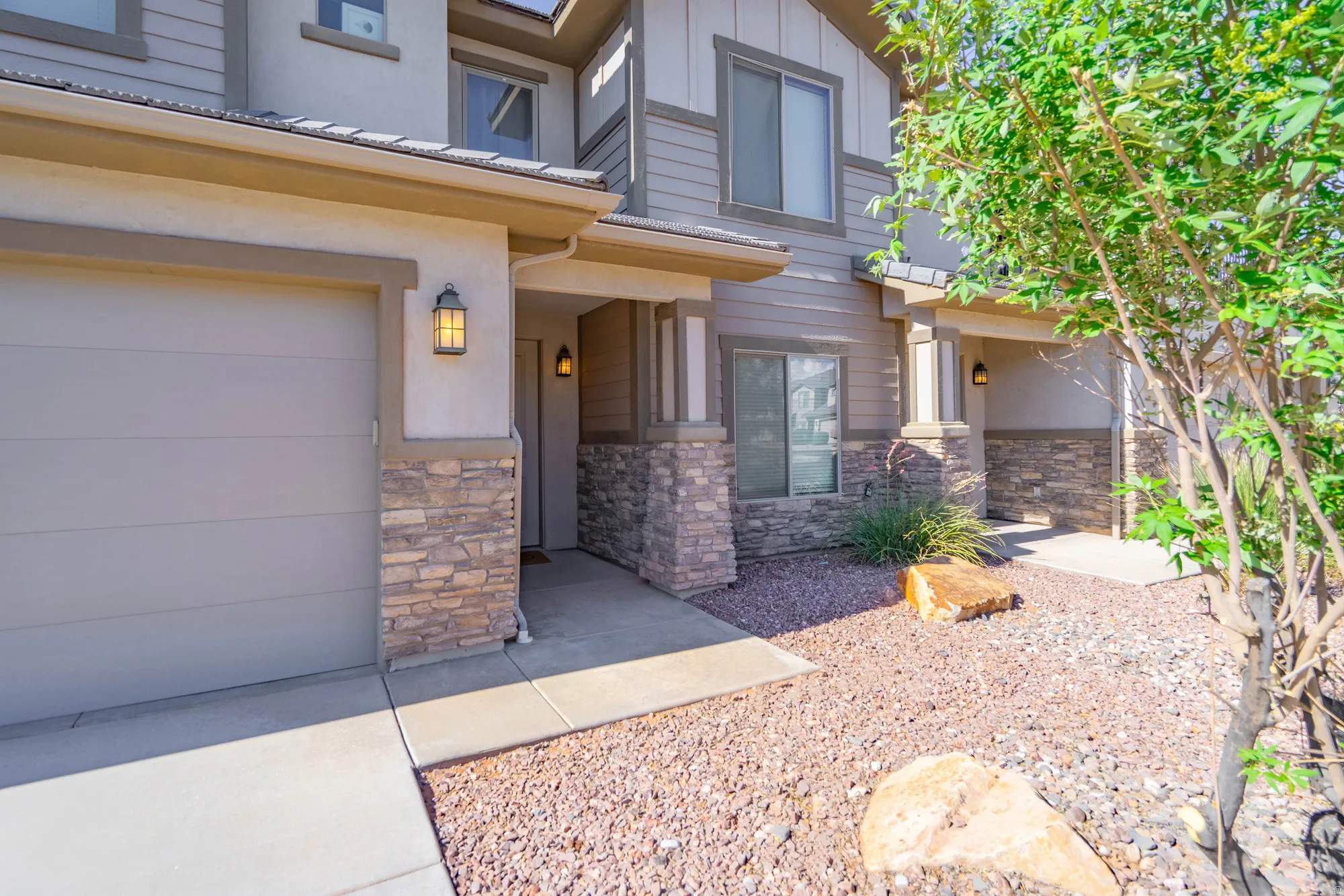 Stone veneer accents, attached garage, exterior lighting fixtures, gravel landscaping, and concrete pathways