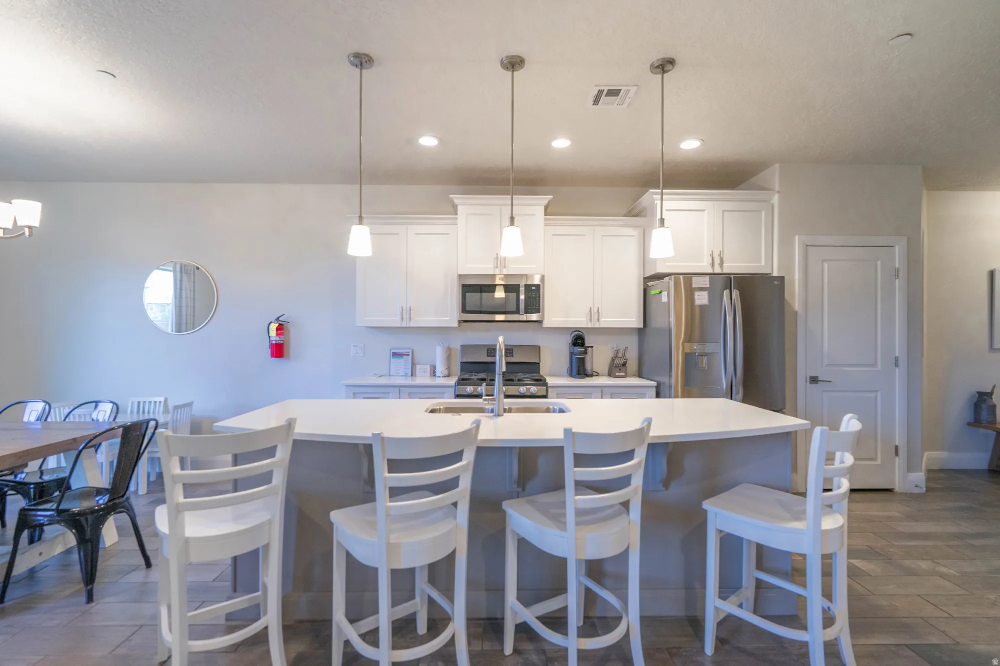 Kitchen featuring an island with built-in sink, white shaker cabinetry, stainless steel appliances, and recessed lighting