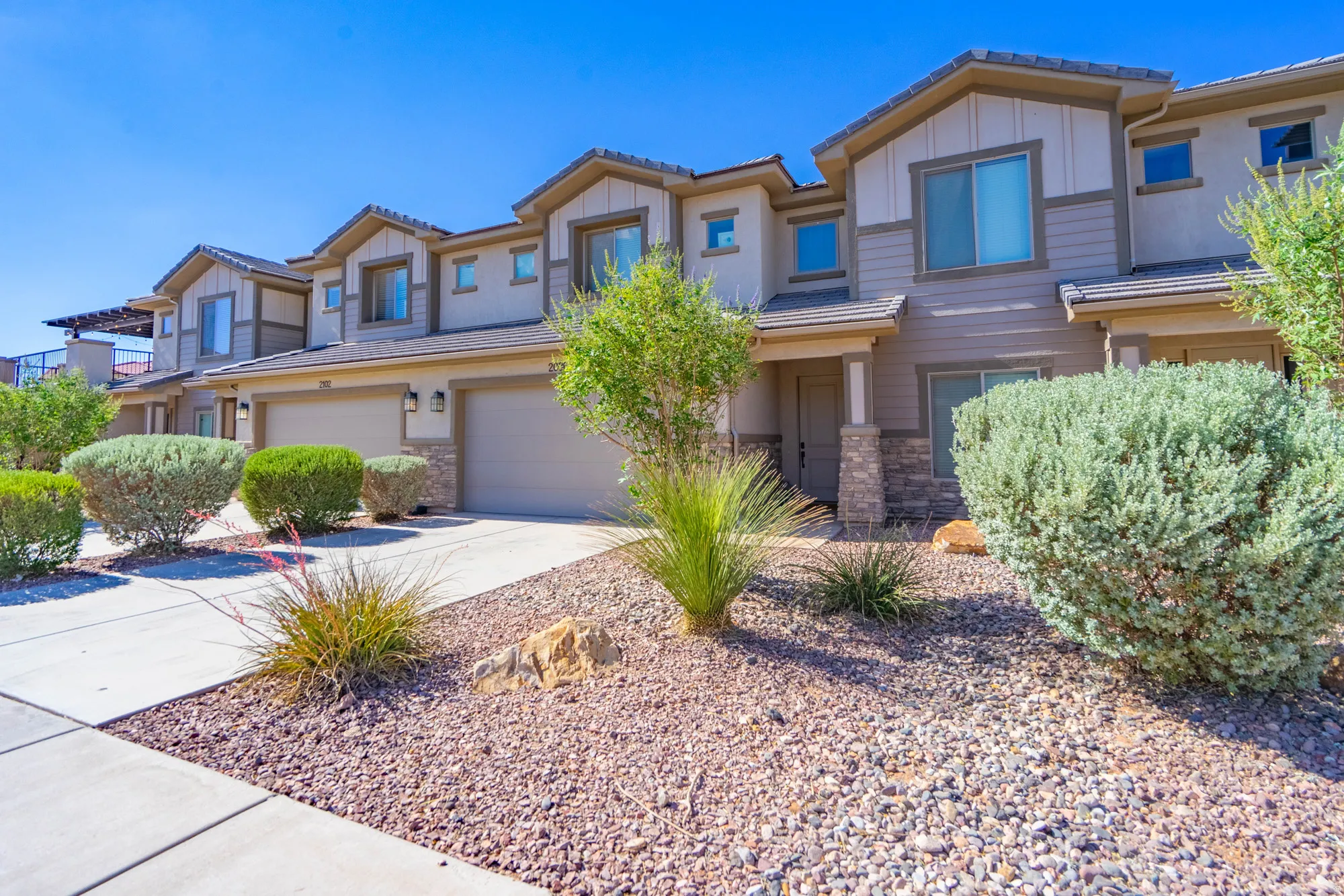 Multi-level townhome exterior featuring an attached two-car garage, stone and stucco facade, concrete driveway, and low-maintenance landscaping