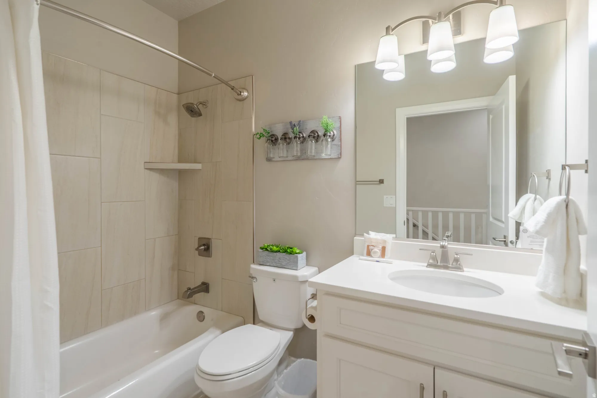 Bathtub with subway tile surround, white vanity with integrated sink, chrome faucet, and overhead lighting fixture