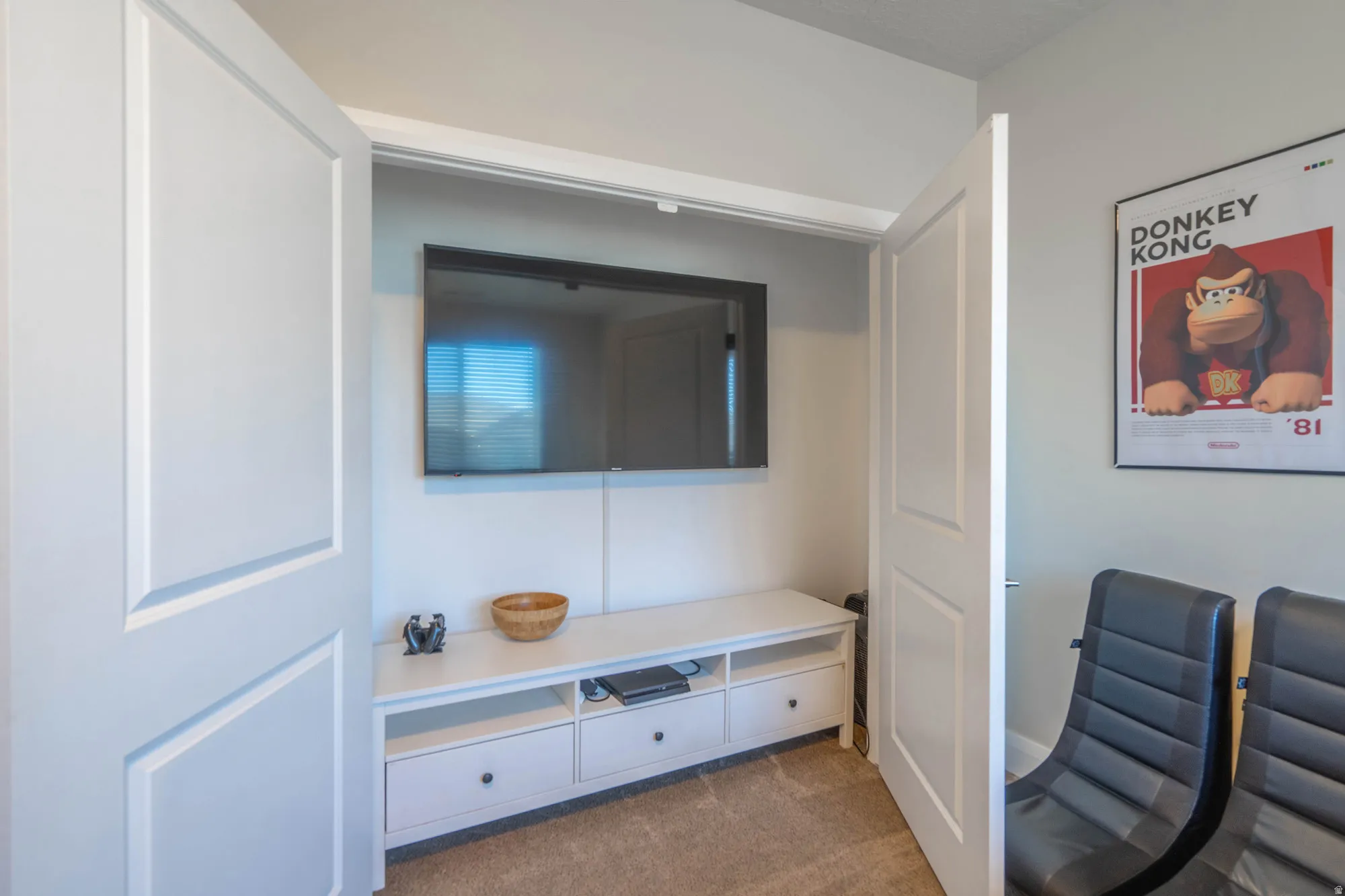 Recessed wall-mounted television, built-in entertainment console with drawers, light-toned carpeting, and a flat-panel interior door