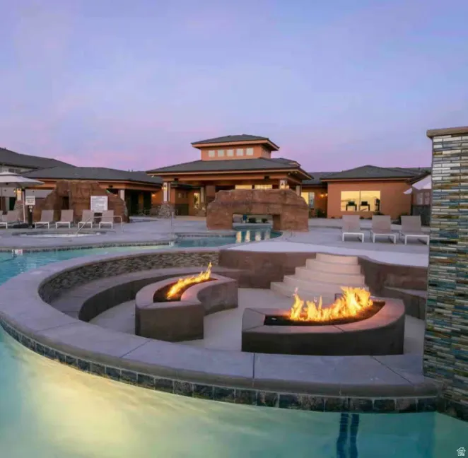 Expansive outdoor pool area featuring built-in fire pits, terraced seating, and a resort-style building with stone accents