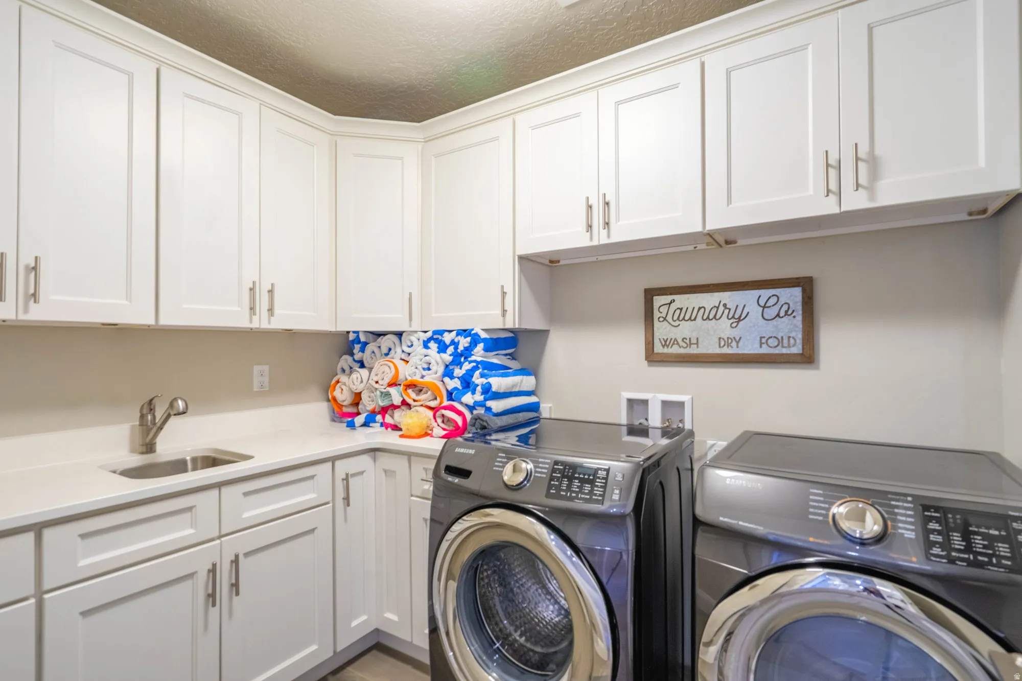 White shaker-style cabinetry, light-toned countertops, stainless steel sink with a gooseneck faucet, and light-colored flooring