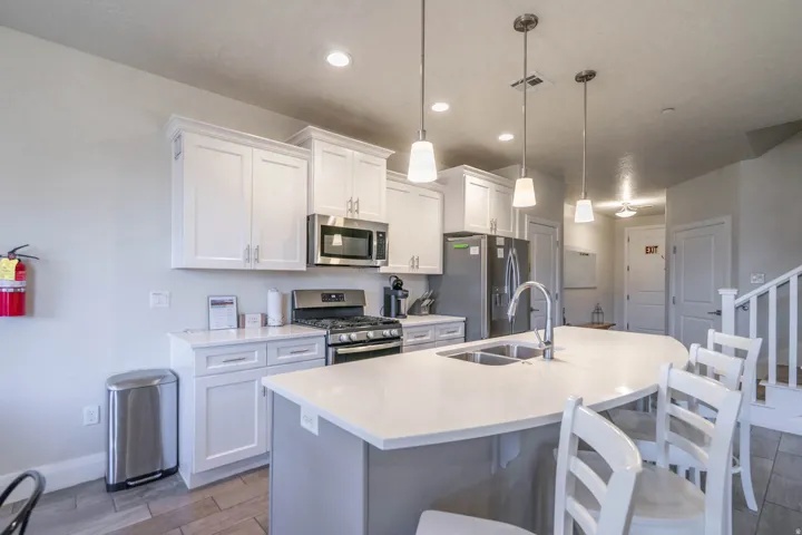 Kitchen featuring stainless steel appliances, white shaker-style cabinetry, a large kitchen island with integrated sink, pendant lighting, and wood-finish flooring