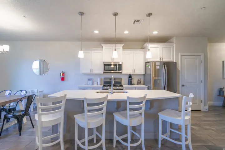 Kitchen featuring an island with built-in sink, white shaker cabinetry, stainless steel appliances, and recessed lighting