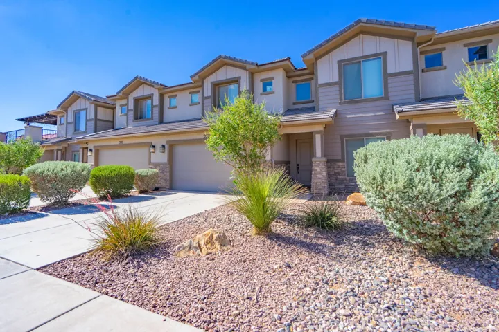 Multi-level townhome exterior featuring an attached two-car garage, stone and stucco facade, concrete driveway, and low-maintenance landscaping