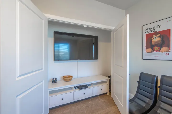 Recessed wall-mounted television, built-in entertainment console with drawers, light-toned carpeting, and a flat-panel interior door