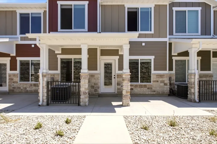 Multi-story exterior with a covered entry, stone veneer and siding facade, concrete patio, and decorative gravel landscaping