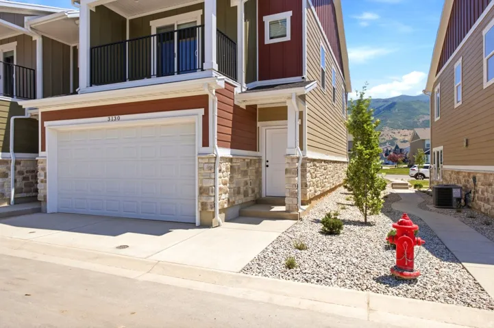 Multi-level residence featuring a panel garage door, stone and siding exterior, and a second-story balcony with metal railings