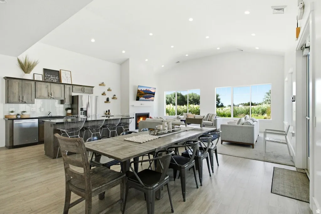 Vaulted ceiling with recessed lighting, integrated kitchen appliances, kitchen island with counter seating, large dining area, and a fireplace with a mantel