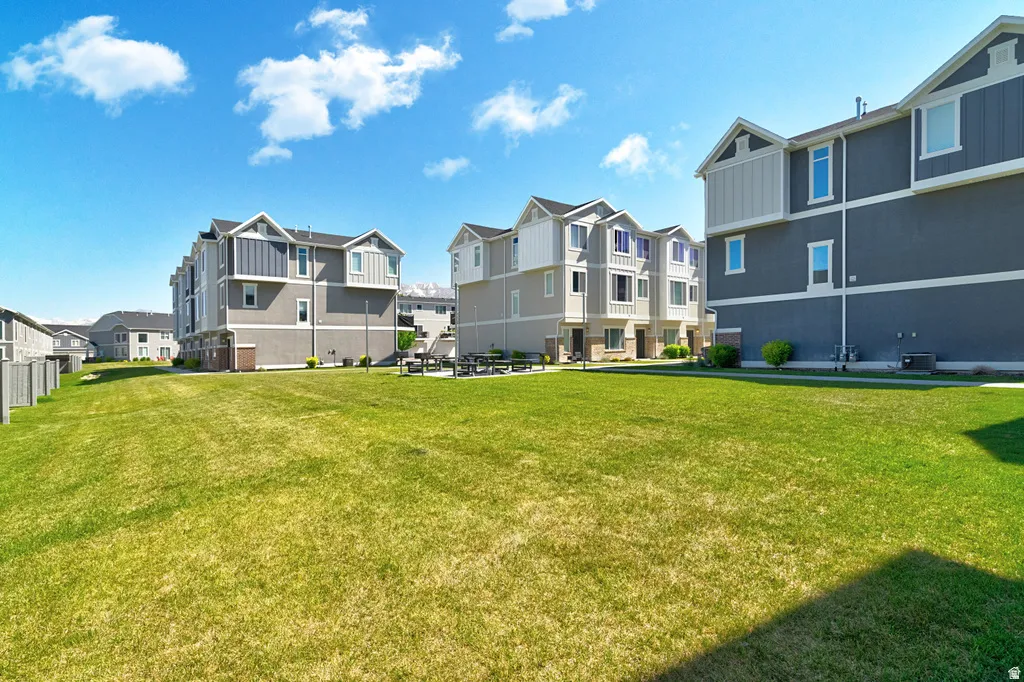 Expansive green space bordered by townhomes with varied facade treatments, multiple windows, and a paved patio with built-in seating