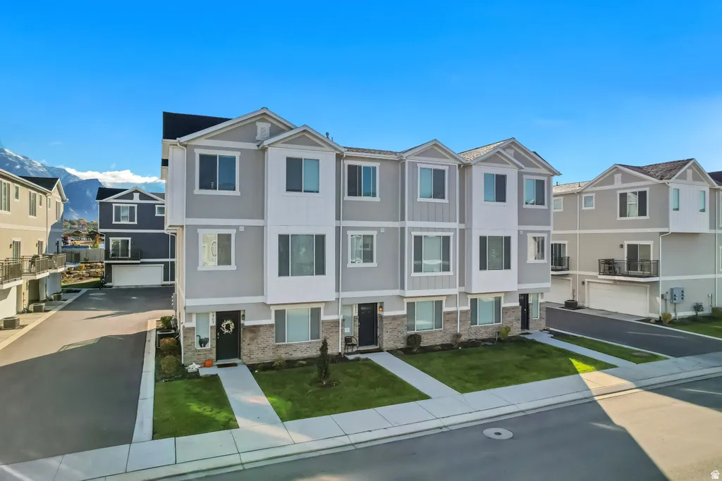 Contemporary multi-story townhomes with light grey siding, dark shutters, and stone-finish accents